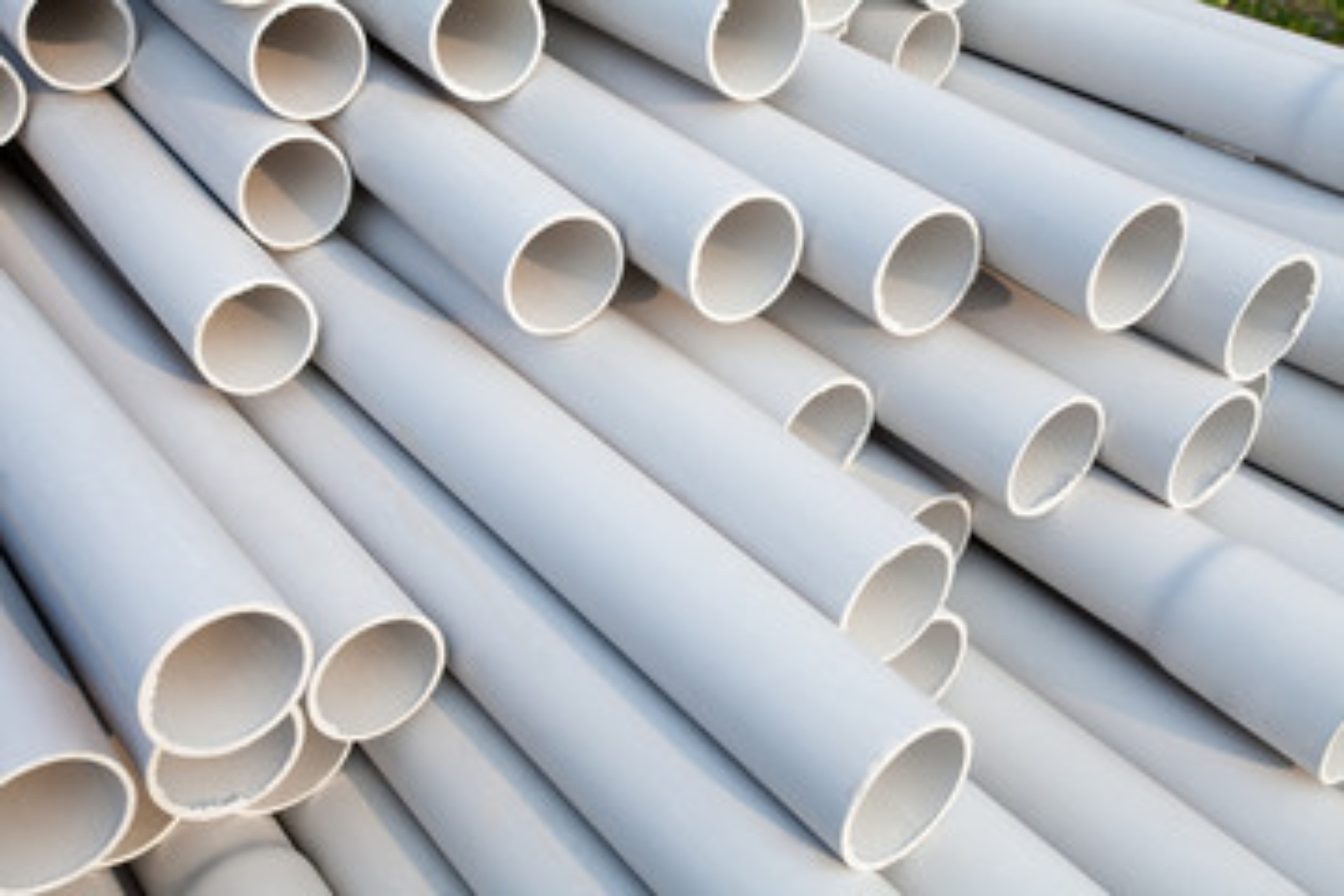Uma pilha organizada de tubos de PVC r&iacute;gido acabados em uma instala&ccedil;&atilde;o de fabrica&ccedil;&atilde;o, demonstrando a estabilidade dimensional e a qualidade da superf&iacute;cie alcan&ccedil;ada ap&oacute;s o processo de extrus&atilde;o.